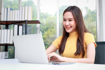 Beautiful smiling Asian female worker sitting in the office using a laptop computer to work. business people concept
