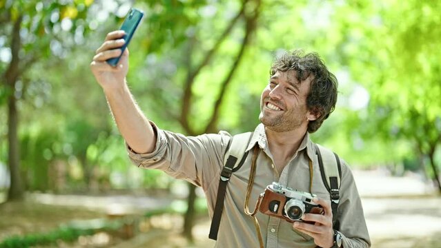 Young hispanic man tourist holding vintage camera make selfie by smartphone at park
