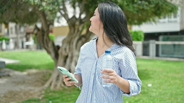 Young chinese woman using smartphone smiling at park