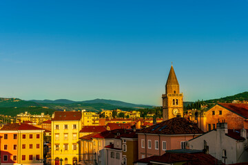amazing evening town with church, tower with bell , yellow houses and beautiful hills with nice...