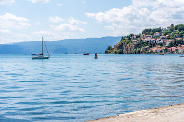 Lake Ohrid North Macedonia with a sailboat on the water and a mountain and city in the background with blue sky and clouds