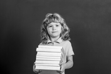 Education and creativity concept. Child holding stack of books with mortar board on blackboard. Back to school. Schoolchild in class. Black and white