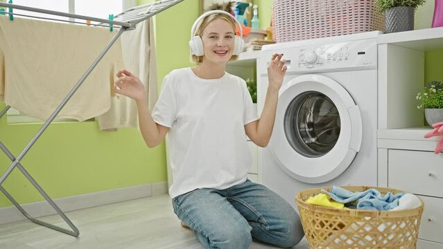 Young blonde woman listening to music and dancing at laundry room