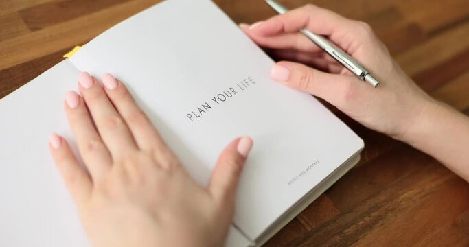 Woman opens white planner and writes down to do list for week. Businesswoman and notebook with Plan Your Life phrase on title page slow motion