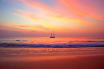 Sailors delight. A sunset captured from the beach, redering the sea,sand and sky red. A single yacht in the distance.