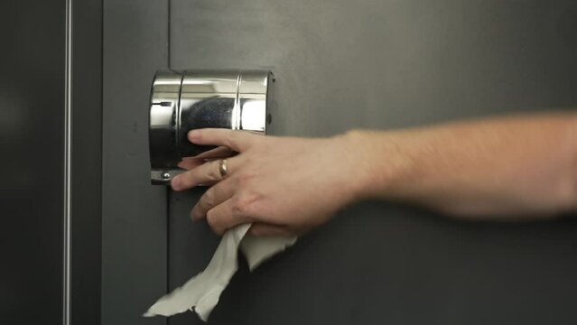 toilet room in dark gray tones
chrome toilet paper holder
close-up man pulls out piece of paper which quickly ends and man gestures with his hand in surprise, opens box to check and spreads his hands