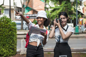 Black tourist woman and Asian backpacker girl sightseeing and taking pictures during summer vacation in Chiangmai, Thailand 