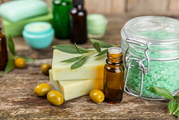 Spa olive. Composition with a jar of natural olive cream, essential oils, sea salt and natural handmade soap with olive and olive sprigs on a brown background. Beauty and relax concept. Flat lay