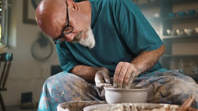 Professional potter creating bowl from clay in workplace using throwing-wheel