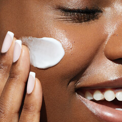 Skin care beauty portrait. Cream smear. Close up portrait of african ametrican woman is applying a...