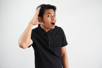 young Asian man looking camera and doing can not hear gesture, trying to listening a gossip wearing black polo t shirt isolated on white background - obrazy, fototapety, plakaty
