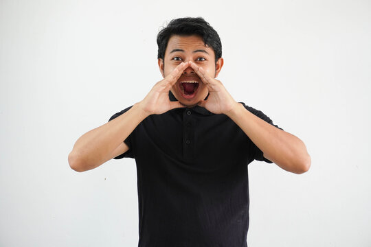 Young Asian man shouting to front with excited face expression wearing black polo t shirt isolated on white background