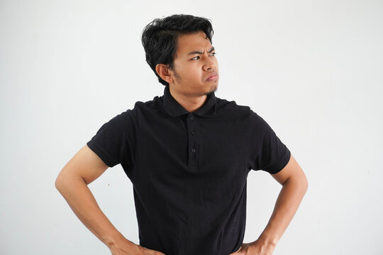 young Asian man showing disappointed expression with both hand on his waist wearing black polo t shirt isolated on white background