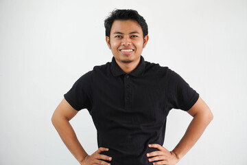 smiling young Asian man showing excited expression with both hand on his waist wearing black polo t...