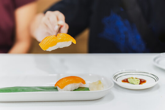 Hand with chopsticks holds sushi with salmon fish.