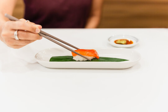 Woman hand with chopsticks holds sushi with salmon fish.