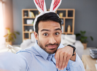 Bunny ears, holiday and selfie with a man and remote work on easter with creative job. Celebration, happy and male professional from Spain feeling silly and goofy with comedy rabbit hat in a home - obrazy, fototapety, plakaty