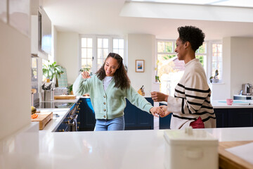 Mother With Teenage Daughter Having Fun Dancing In Kitchen At Home Together