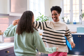 Mother With Teenage Daughter Having Fun Dancing In Kitchen At Home Together