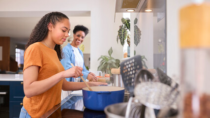 Mother With Teenage Daughter Helping To Prepare Meal At Home In Kitchen Together