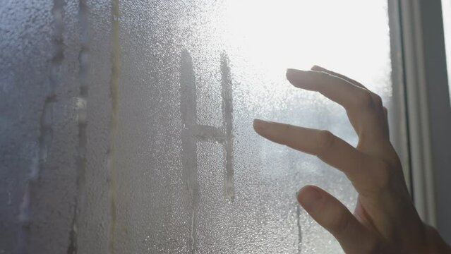 A woman writes hello on a misted glass with her finger and draws a smiley close-up