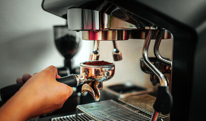 Hands of barista holding portafilter to prepare coffee at automatic coffee machine in cafe