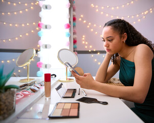 Unhappy Teenage Girl At Home In Bedroom Getting Ready For Prom Or Night Out Looking At Mobile Phone © Monkey Business