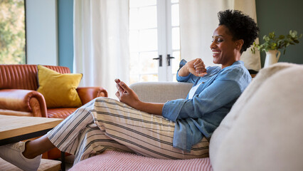 Mature Woman Relaxing On Sofa At Home Looking At Mobile Phone