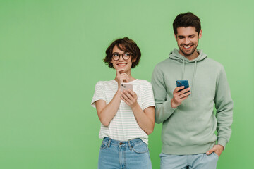 Smiling man and woman using mobile phones isolated over green wall