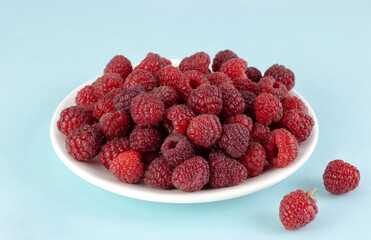 Fresh raspberries in a wooden bowl on a blue background.