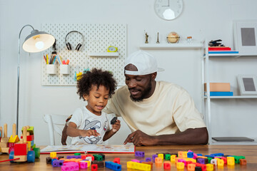 black father teaching his son how to read and watching his children play jigsaw puzzles to enhance...