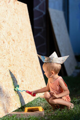 Little blond boy plays builder.Kid in T-shirt, shorts and garrison cap holds a construction...