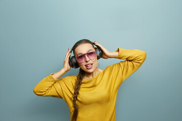 Beautiful young woman in headphones listening to music on blue background