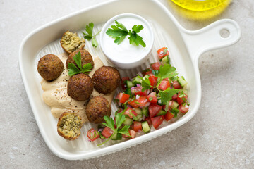Beige serving tray with falafel, hummus, tomato salsa and yogurt, horizontal shot, elevated view