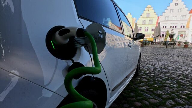 Power cable connected with a charger plugged into a black electric car, traditional northern European city in the background blurred
