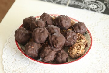 Homemade candy made from nuts and dried fruits. Some are covered in chocolate. They lie on a plate.