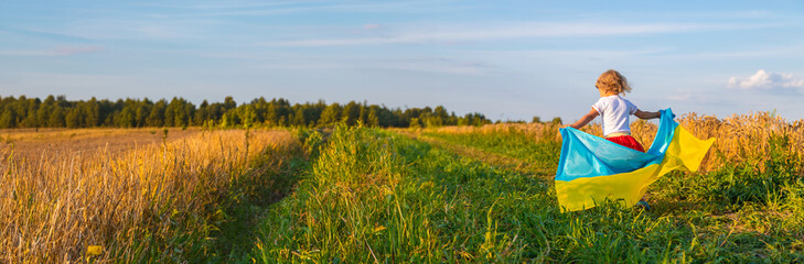 Obraz premium Child in a field of wheat with the flag of Ukraine. Selective focus.