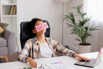 The concept of a lot of work. Tired Indian student girl sleeping with stickers on her eyes while sitting at the table. Distracted woman in home office.