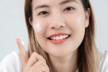 Fototapeta premium Beautiful Asian woman smile use cream for good skin. face of a healthy woman apply cream and makeup. Advertisement for skin cream, anti-wrinkle, baby face, whitening, moisturizer, tighten pores serum