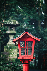Wooden lantern and stone lantern in woodland, Japan. The traditional lamps often light pathways leading to Shinto shrines or temples.