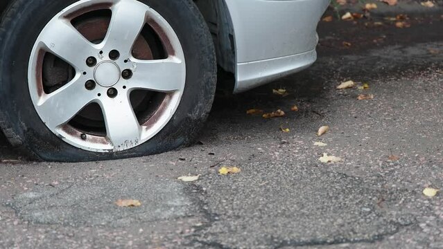 Close-up of a flat front tire on a silver car. Broken car parked on the street.