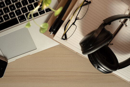 Top view of office Workplace with open laptop, a blank open note book, a smart phone ,a pen, a specs and a head phone on a wooden desk