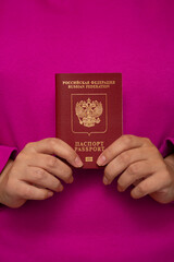 Vertical photo. White woman holds red Russian biometric passport on pink background. Patriotism and Fatherland. Concept of immigration from Russia, obtaining citizenship, travel, tourism, trip. 