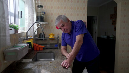 Stressed senior man leaning on kitchen sink struggling in despair at home, older person suffering breakdown crisis alone in solitude, depression and anxiety concept in old age