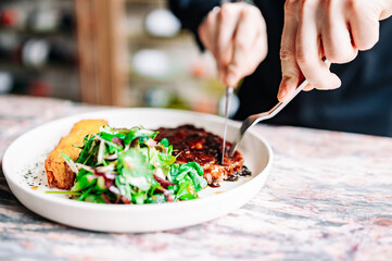 man hands with fork and knife eating beef steak and salad in cafe