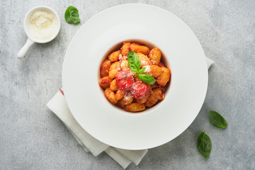 Potato gnocchi. Traditional homemade potato gnocchi with tomato sauce, basil and parmesan cheese on kitchen table on light grey kitchen table background. Traditional Italian food. Top view.