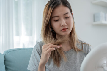 Asian woman very sad and upset looking at damaged hair, hair loss, hair thinning problem, vitamin...