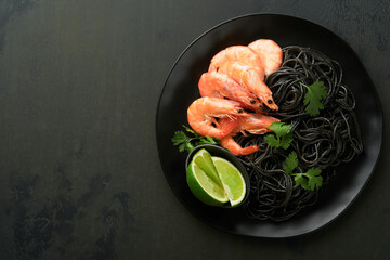Black spaghetti pasta shrimp on black plate on dark concrete table background. Squid ink pasta with prawns. Pasta seafood. Top view on black stone table. Mediterranean traditional cuisine dish.