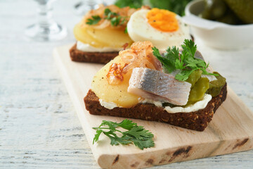 Open sandwich or smorrebrod with rye bread, herring, eggs, caramelized onions, parsley and cottage cheese on old wooden rustic table backgrounds. Danish or Scandinavian traditional food snack lunch.