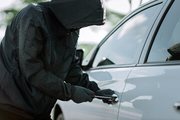 Man dressed in black holding screwdriver to break lock and steal a vehicle on the road, Social destruction, Insurance, Car thief concept.